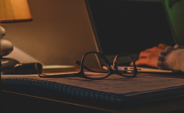 Person in amber blue light blocking glasses for sleep working at a dim evening desk