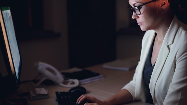 Person wearing blue light blocking glasses for sleep while working at a computer in the evening