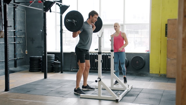 person performing full body workout squat exercise in gym with barbell and weights